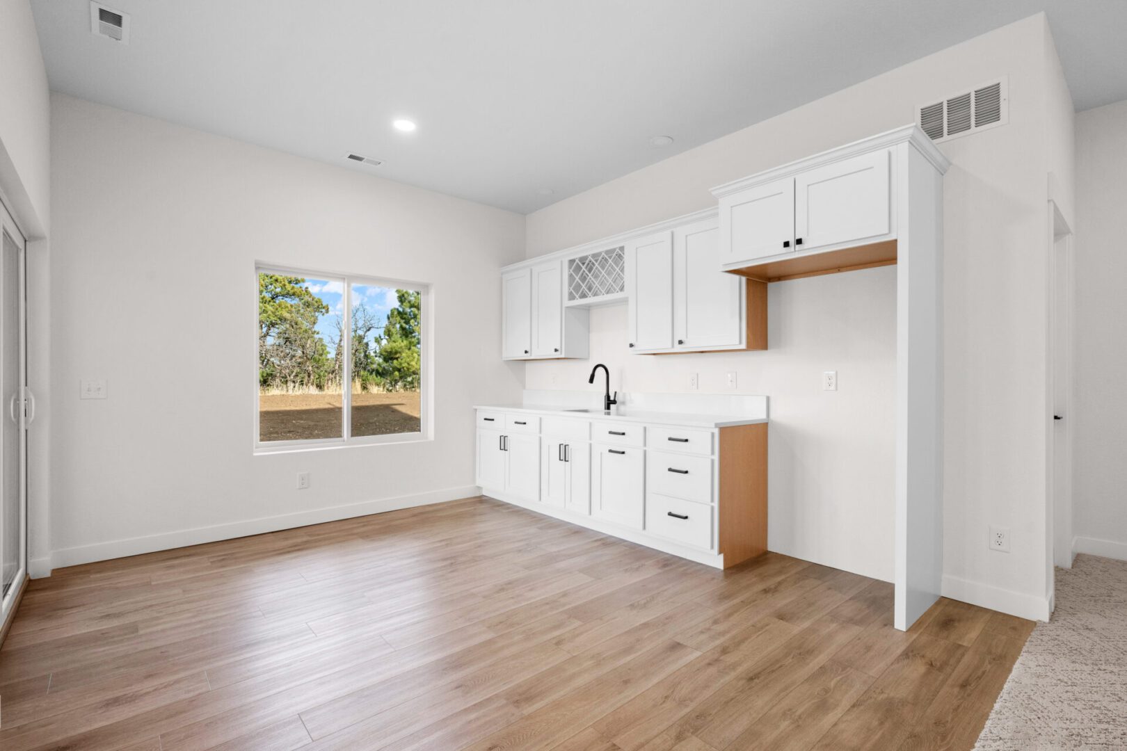 Bright, empty kitchen with white cabinets and wooden flooring.