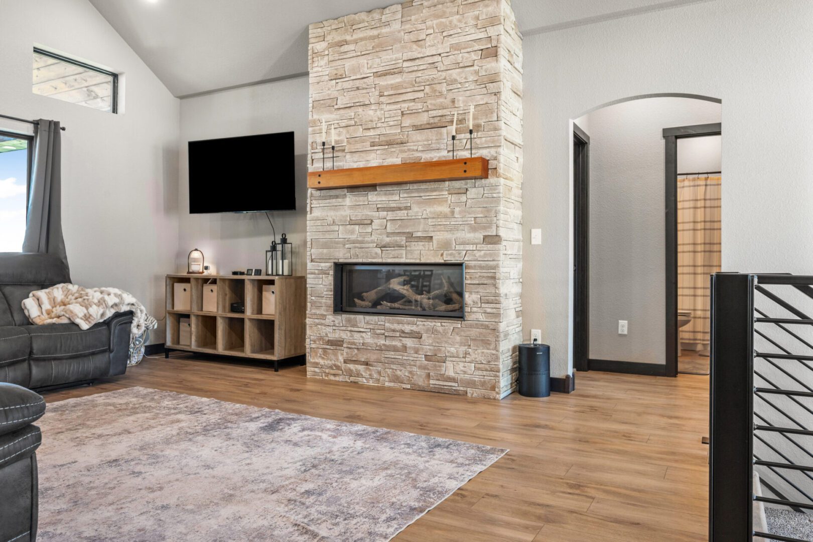 Modern living room with stone fireplace and wooden floor.
