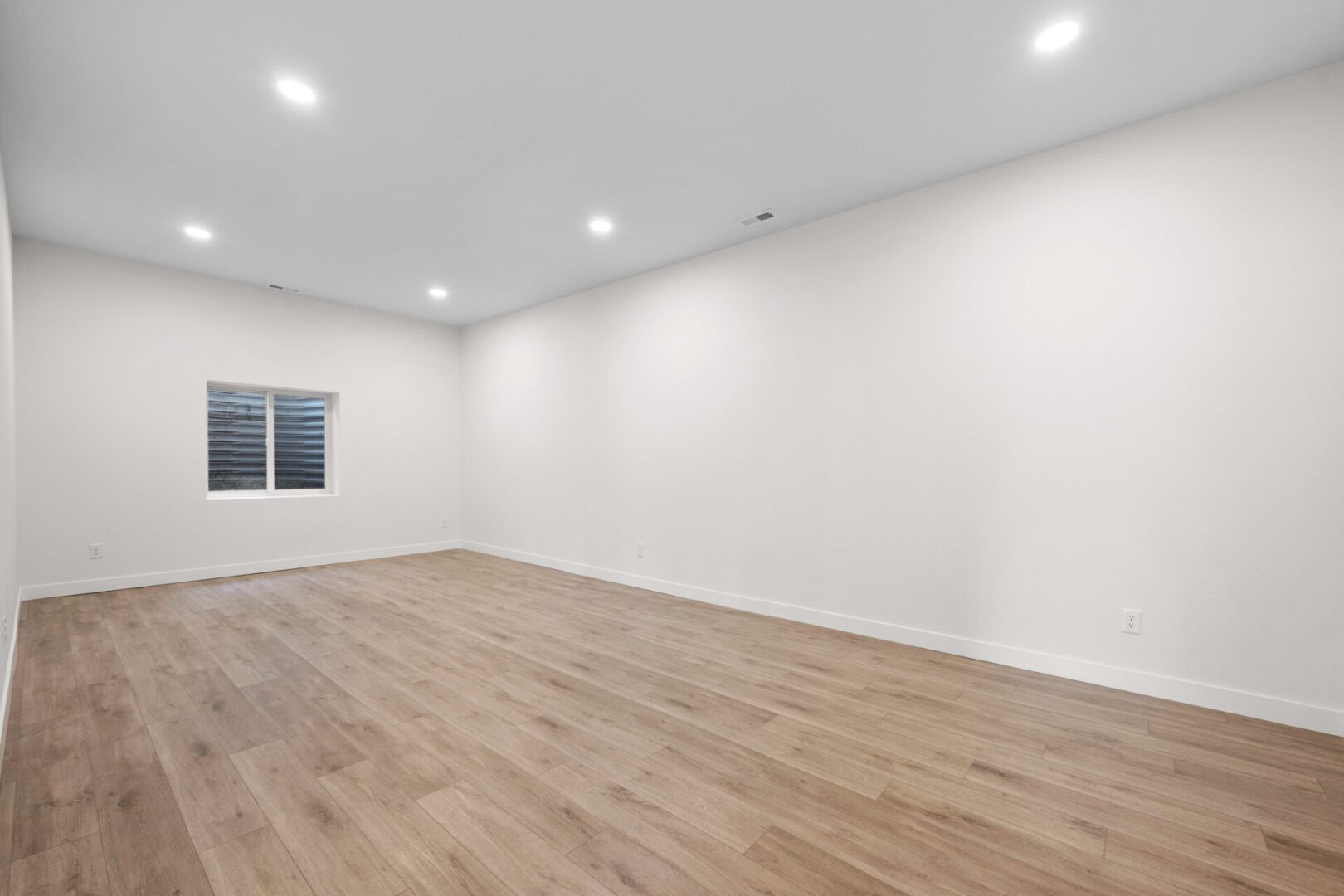Empty room with white walls and wooden flooring under recessed lighting.