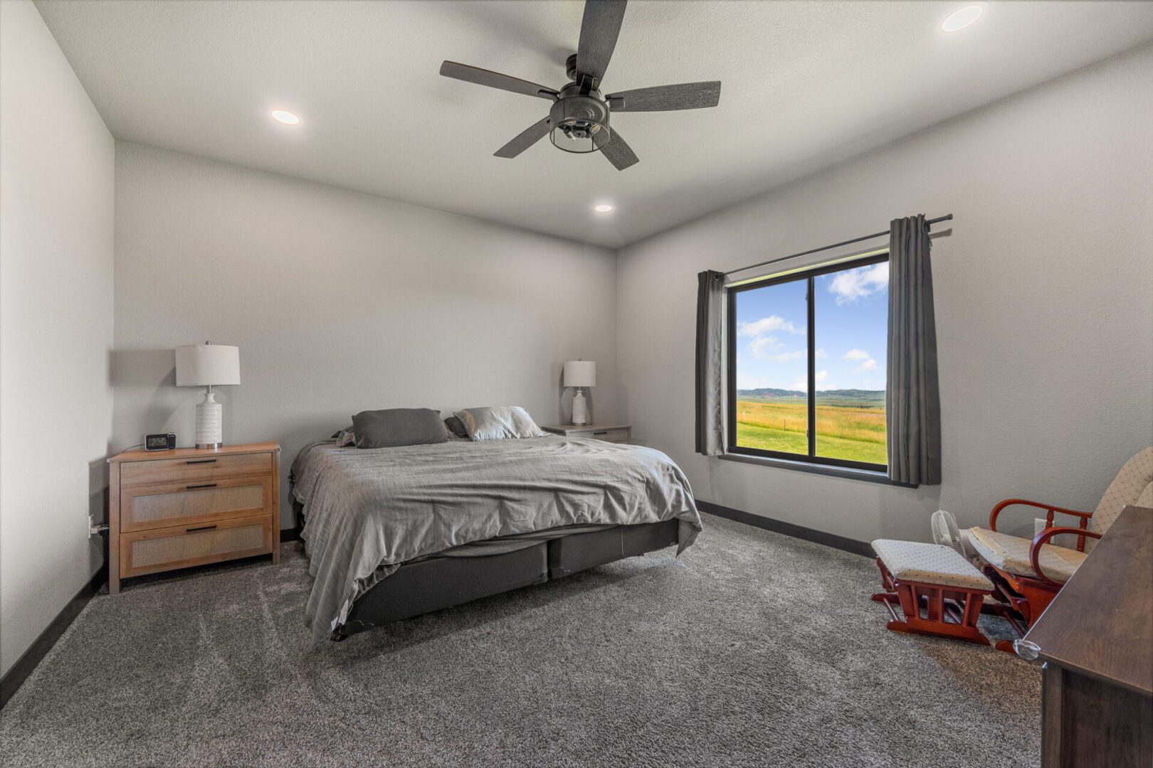 Modern bedroom with gray carpet and large window showing green landscape.