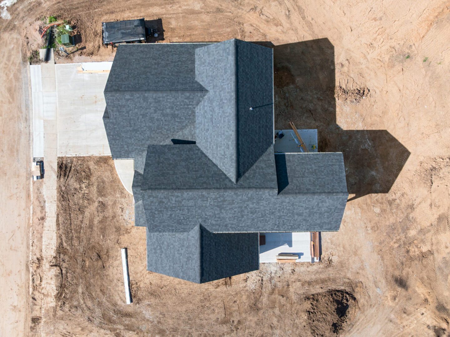 Aerial view of a large house with a complex roof design and surrounding barren ground.