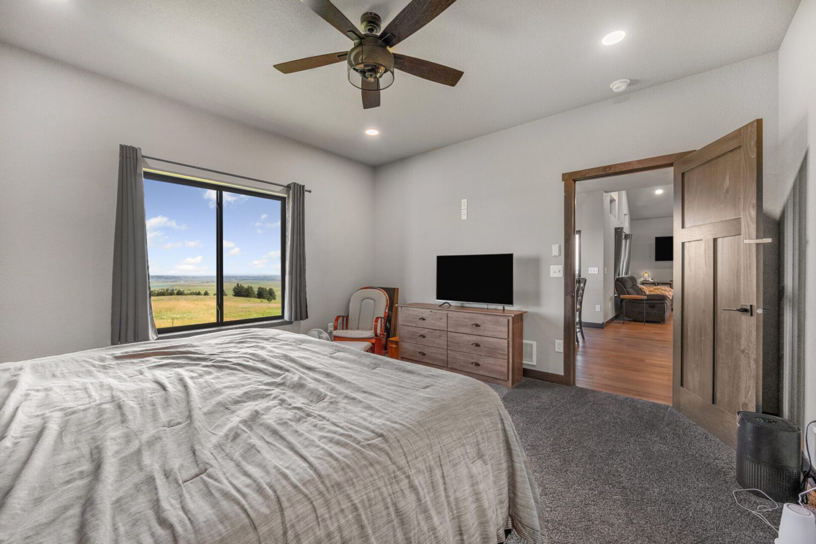 Cozy bedroom with carpet, ceiling fan, and TV overlooking green fields.