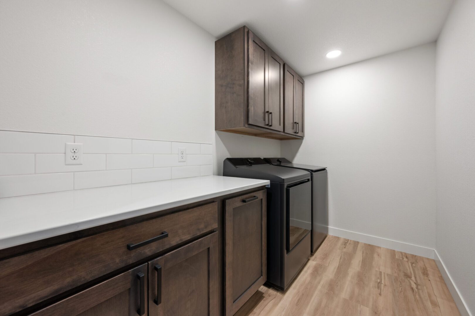 Modern laundry room with dark wood cabinets and front-loading washer and dryer.