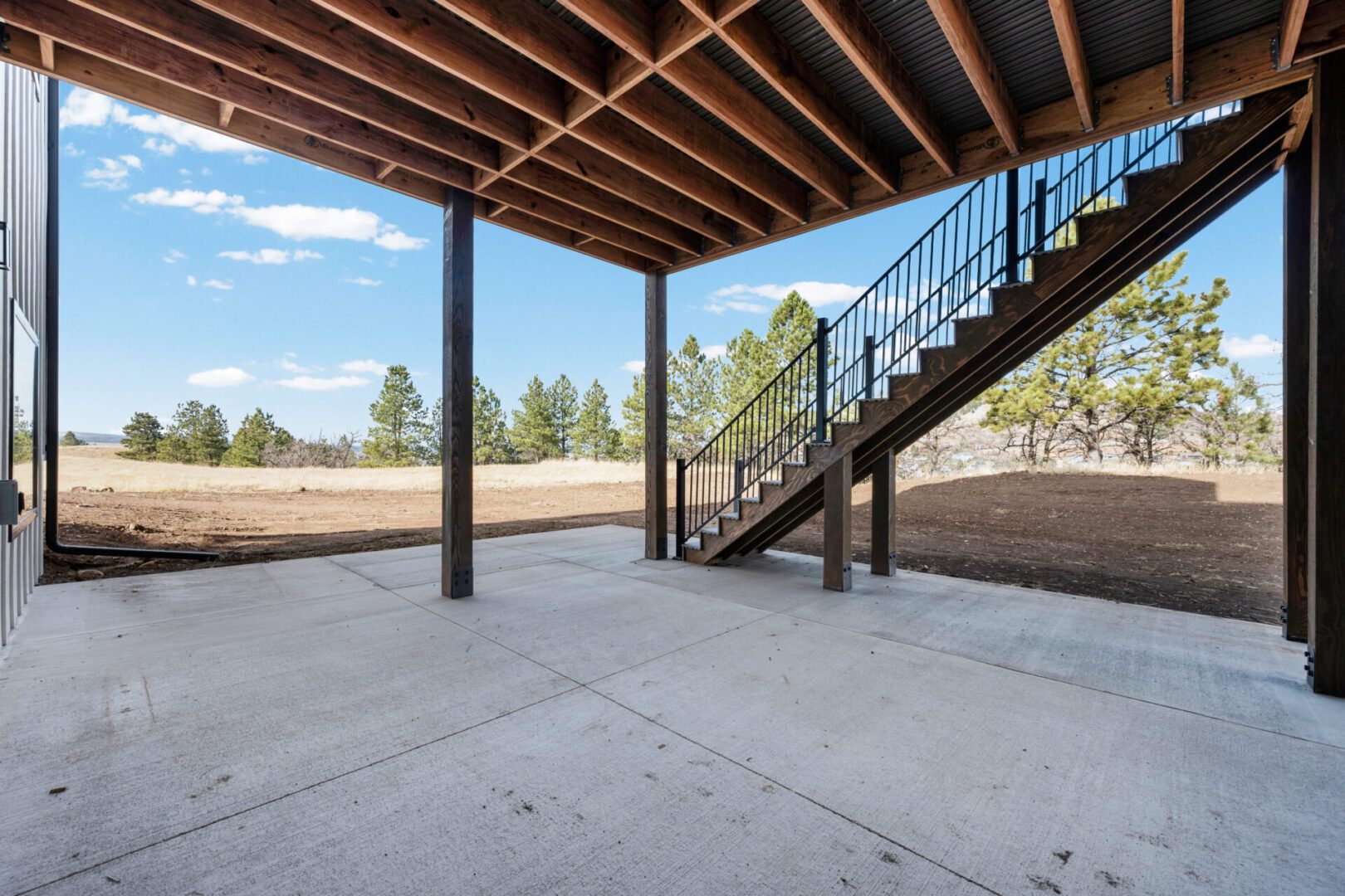 Covered outdoor patio with concrete floor and metal staircase.