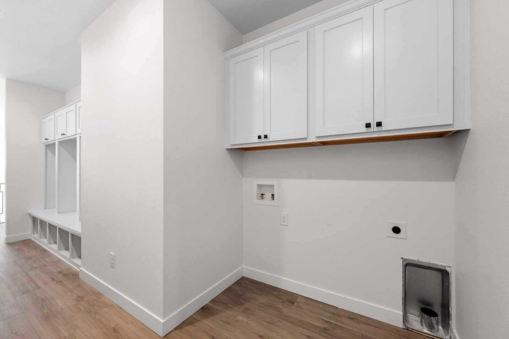 Empty laundry room nook with white cabinets and wooden floor.