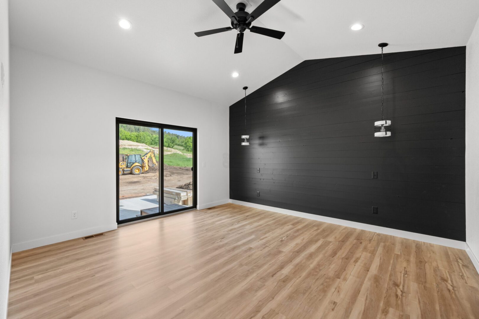 Modern empty room with wood flooring and black accent wall.