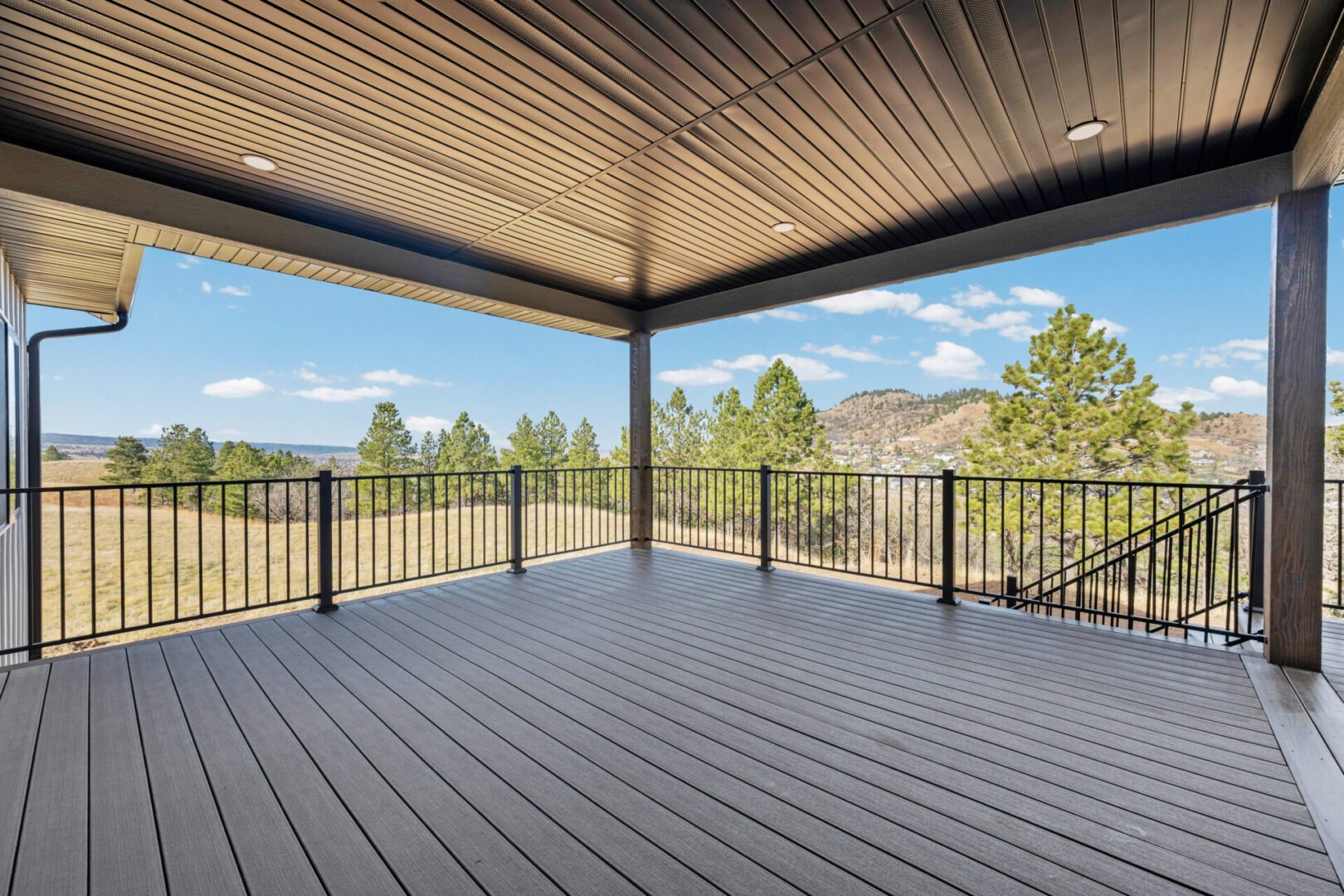 Spacious covered deck with railing overlooking a scenic forest view.