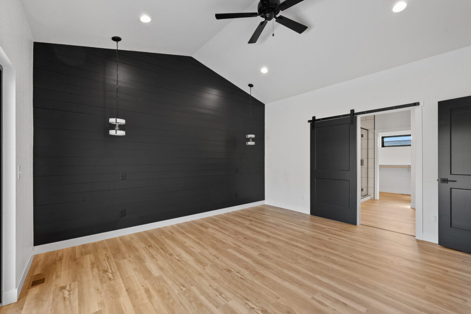 Empty modern room with black accent wall and wooden floor.