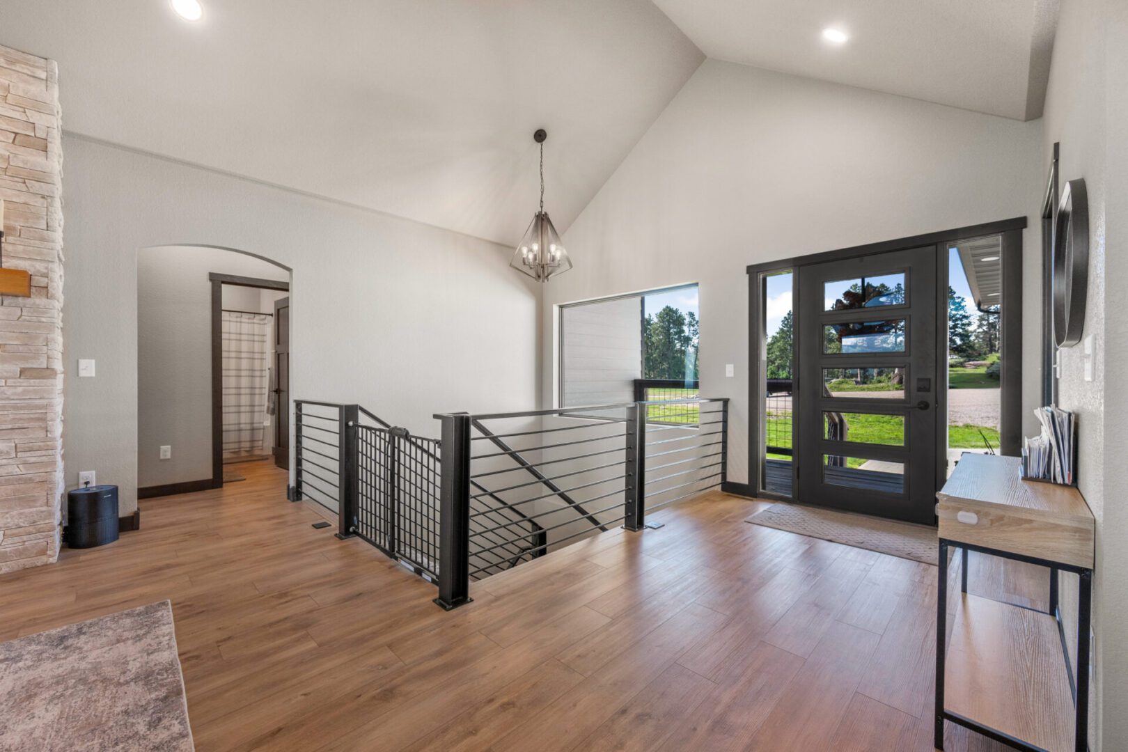Spacious modern entryway with wooden floors and black metal stair railing.