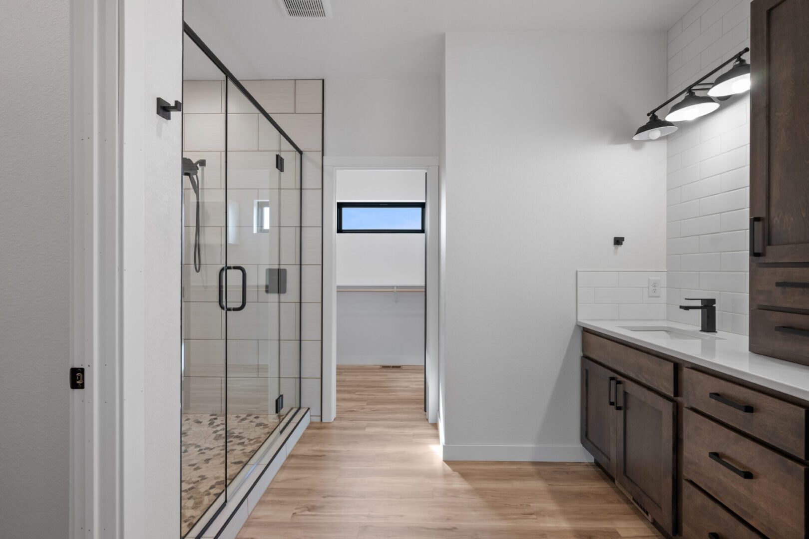 Modern bathroom with glass shower and wooden floor.