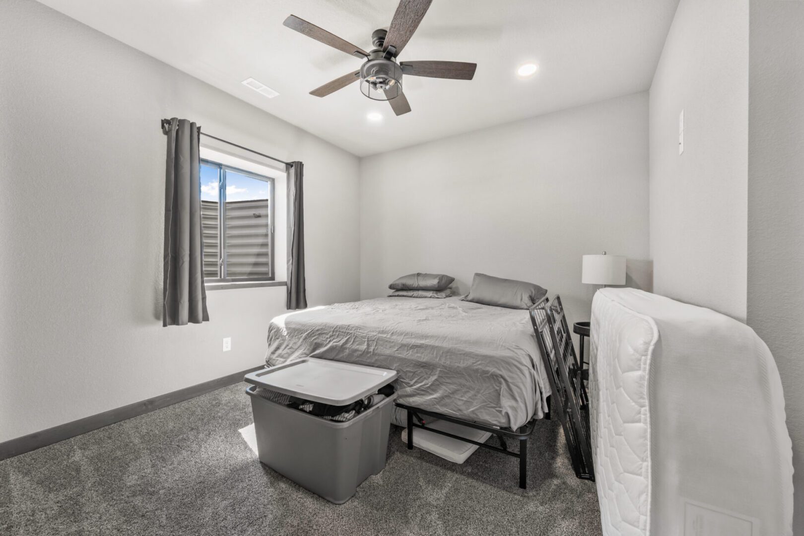 Minimalist bedroom with gray bedding and ceiling fan.