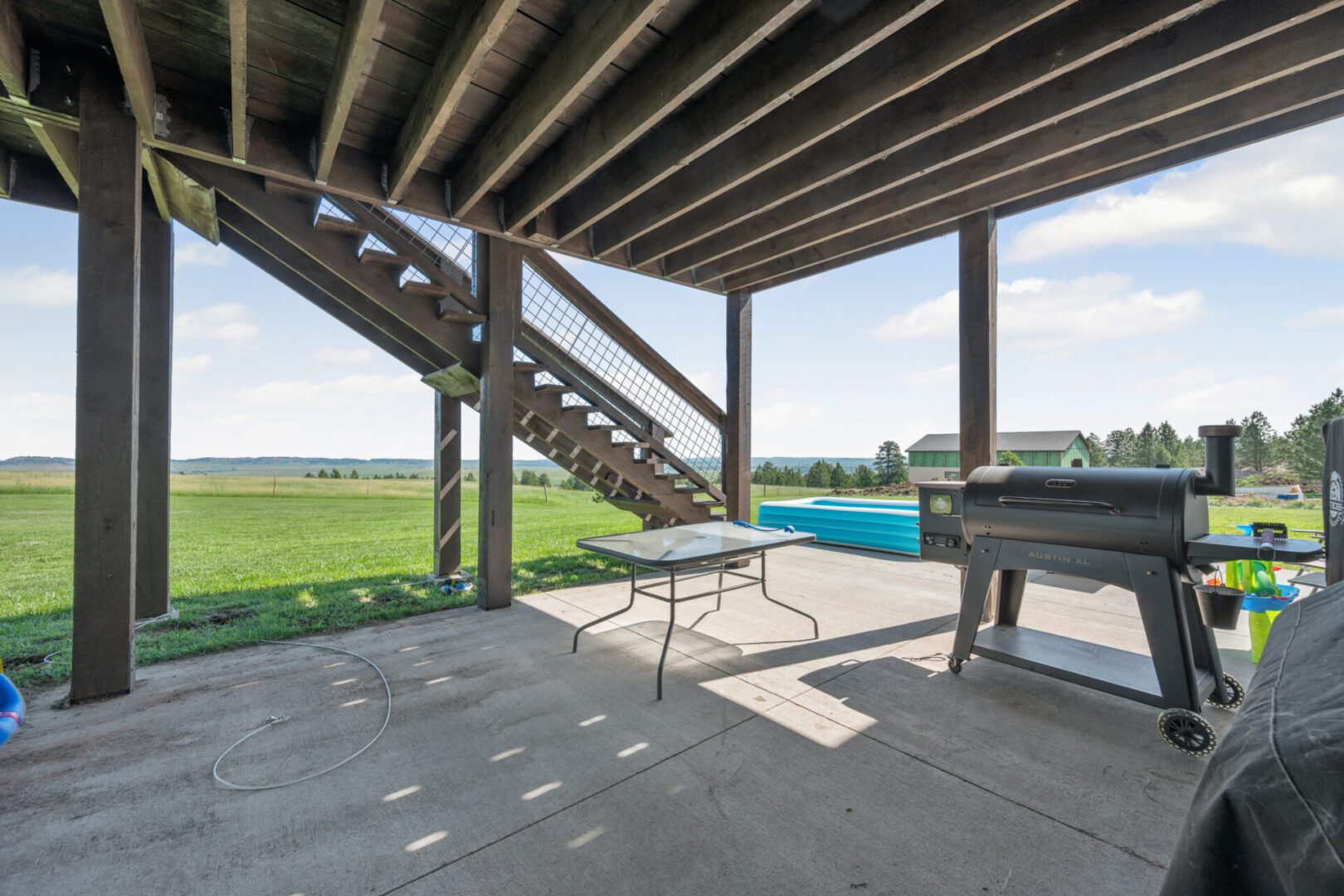 Covered patio with stairs, grill, and pool view.