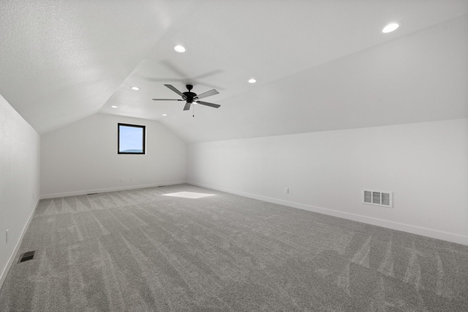 Spacious empty room with gray carpet and ceiling fan.
