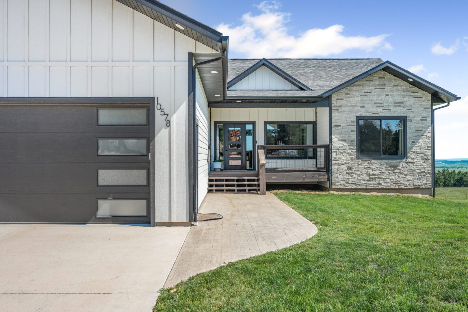 Modern home exterior with stone and siding, featuring a glass-paneled garage door and a covered porch.