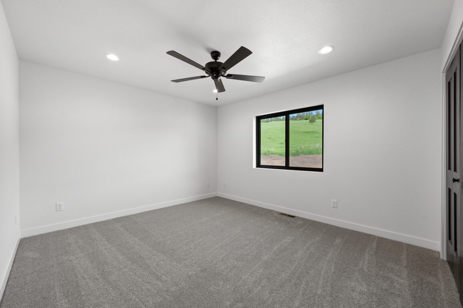Empty room with gray carpet, white walls, black ceiling fan, and window.