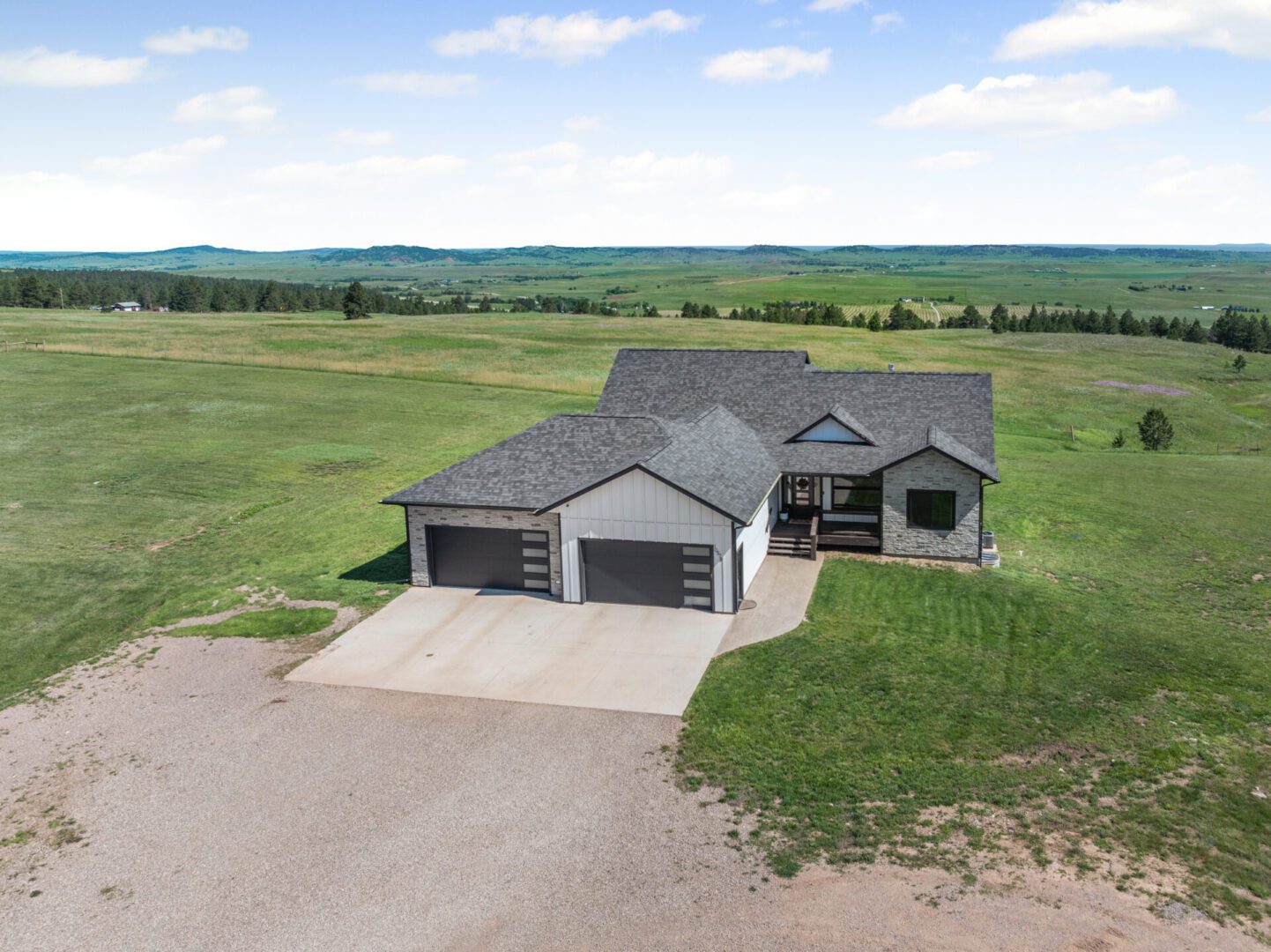 Modern single-story house with a three-car garage surrounded by open green fields.