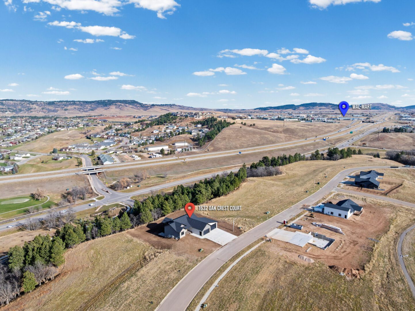 A scenic aerial view of a suburban area with houses, roads, and open land under a partly cloudy sky.
