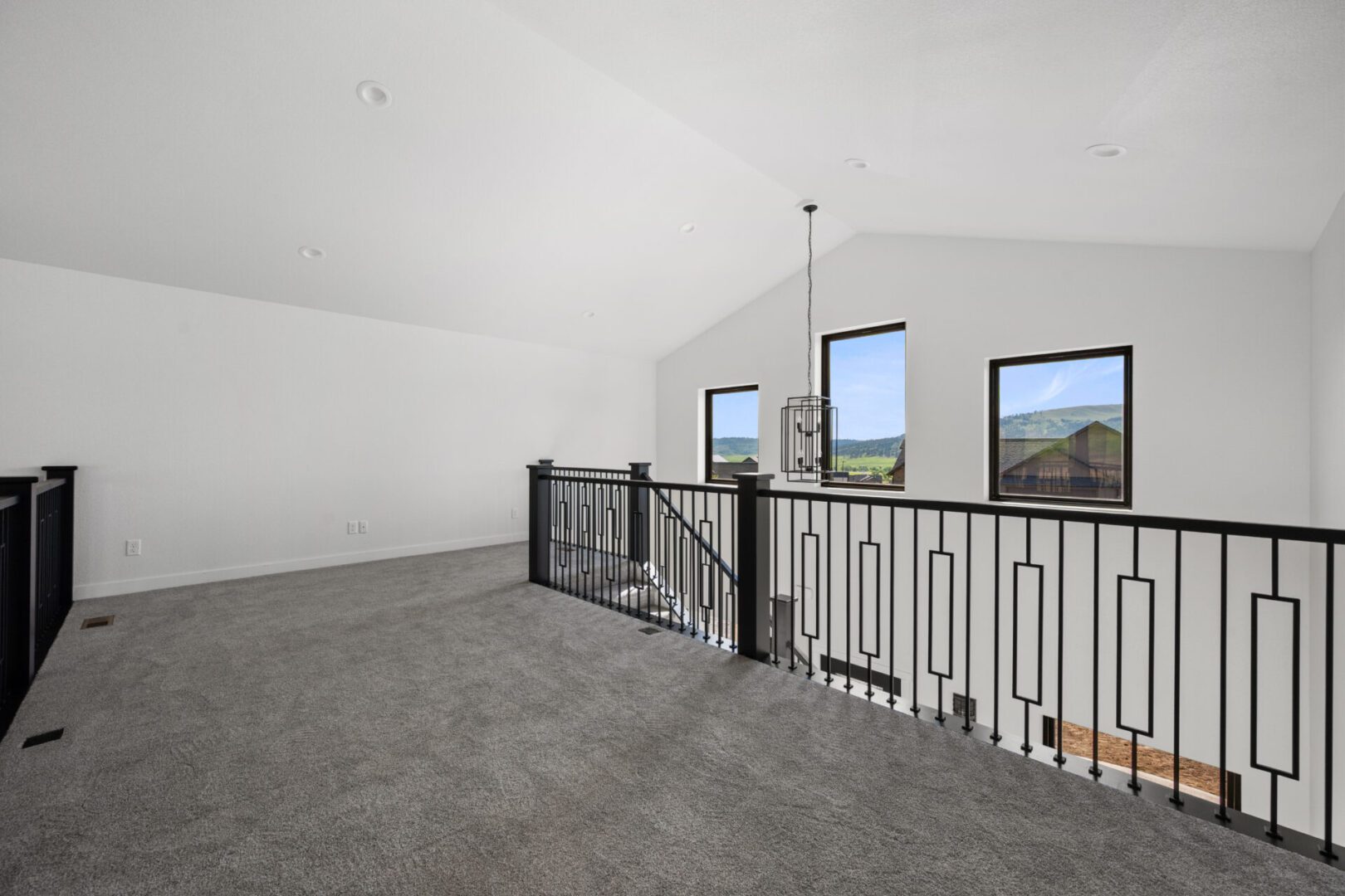 Spacious empty room with carpet and black railing overlooking large windows.