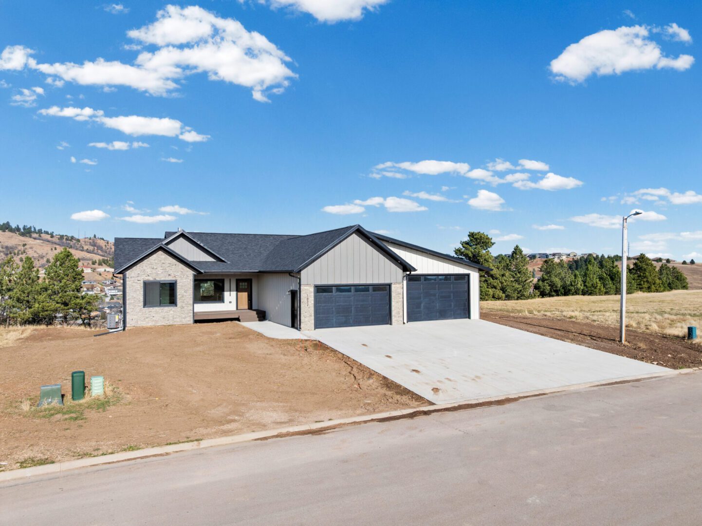Modern single-story house with a large driveway and three-car garage under a blue sky.