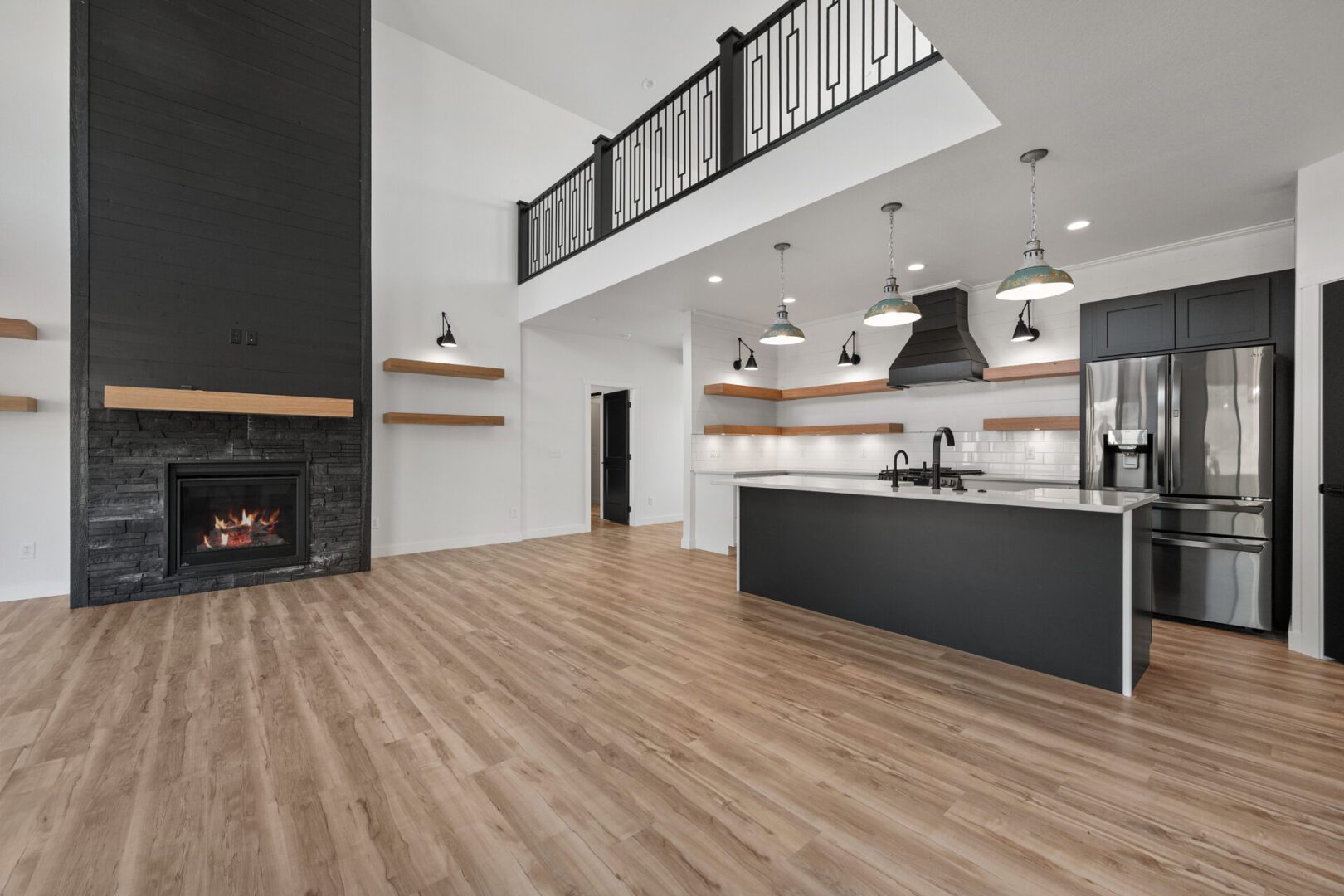 Modern kitchen with wooden floor and black island under pendant lights.