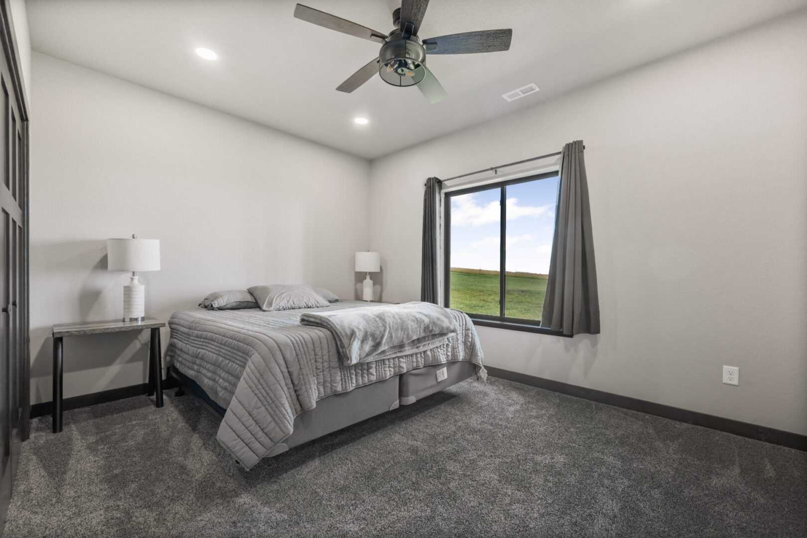 Bright bedroom with gray carpet, bed, and ceiling fan.