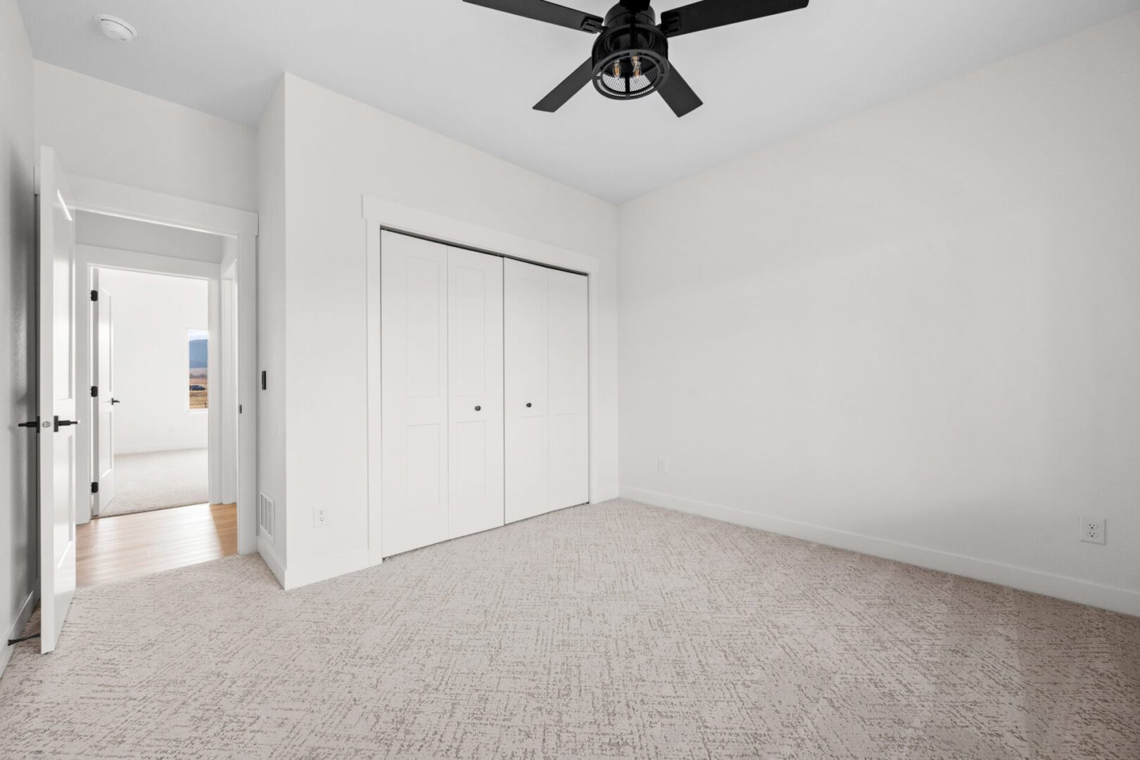 Empty bedroom with carpet, white walls, and double closet doors.