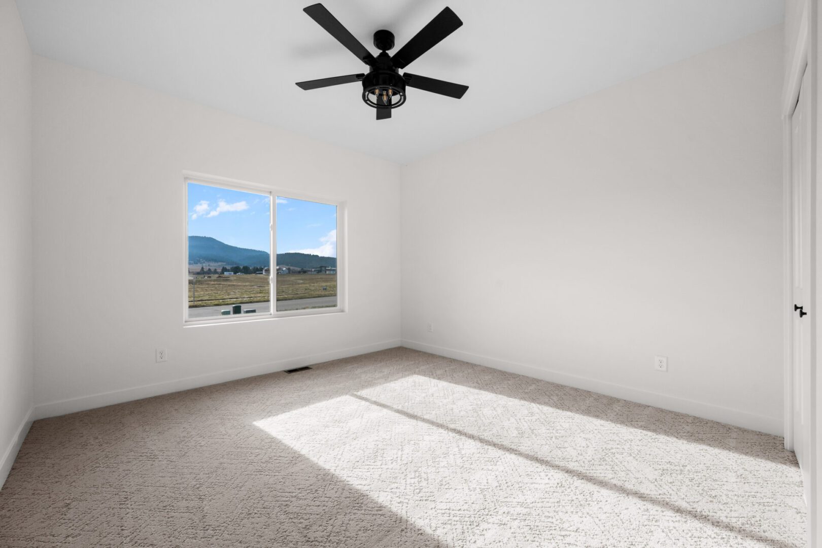 Empty room with carpet and ceiling fan overlooking mountains.