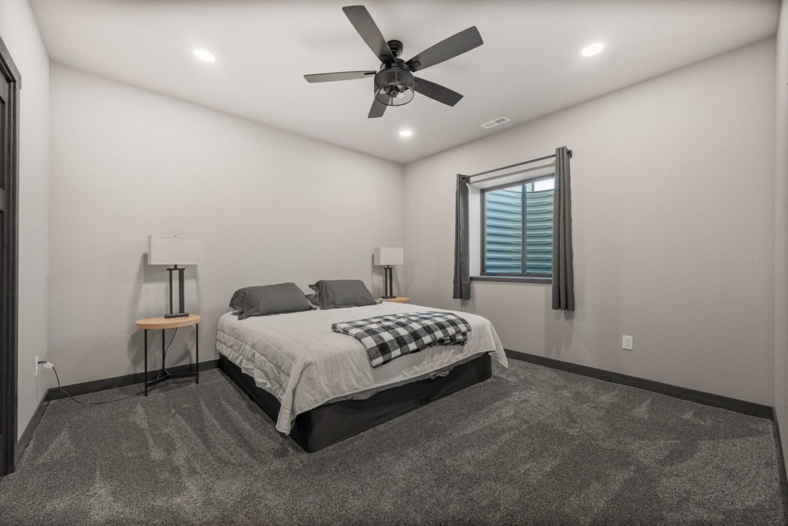 Minimalist bedroom with a gray carpet and ceiling fan.