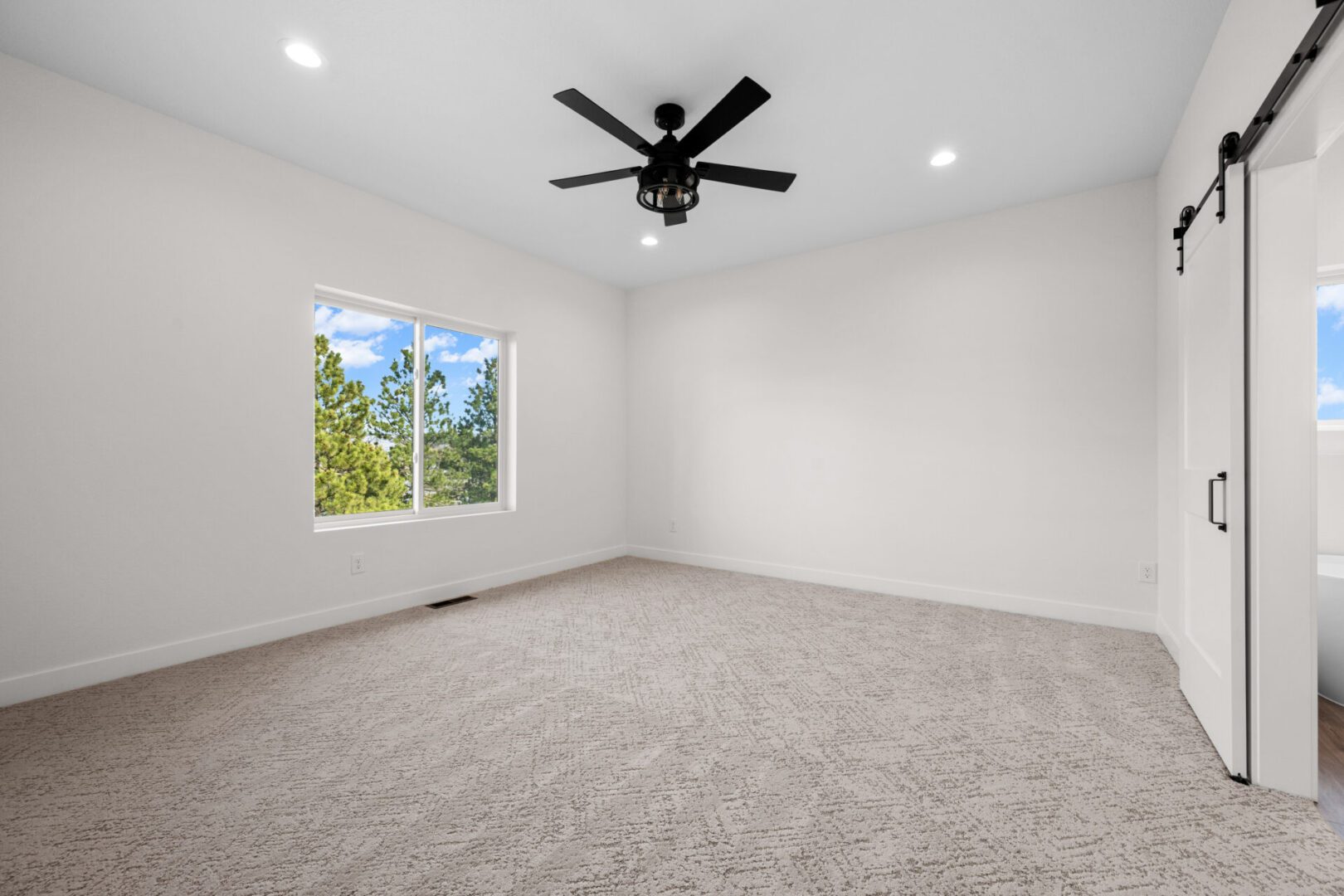 Empty carpeted room with large window and black ceiling fan.