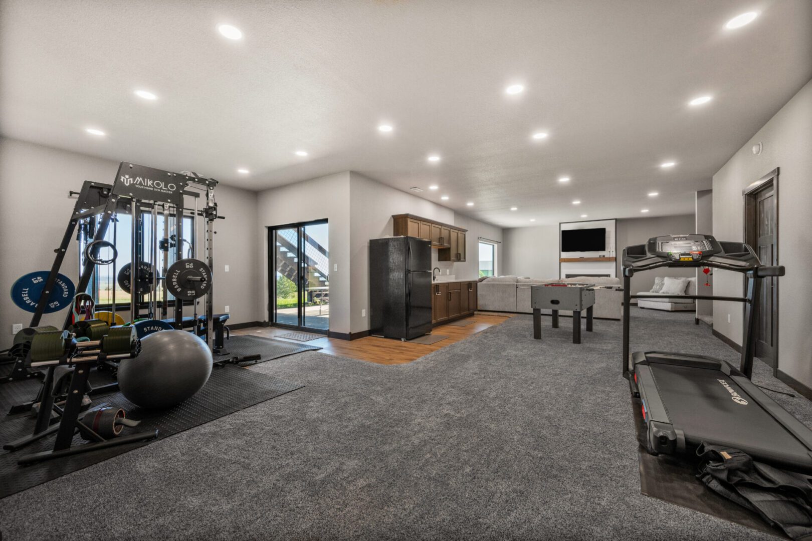 Modern home gym with large windows, workout equipment, and a cozy seating area.