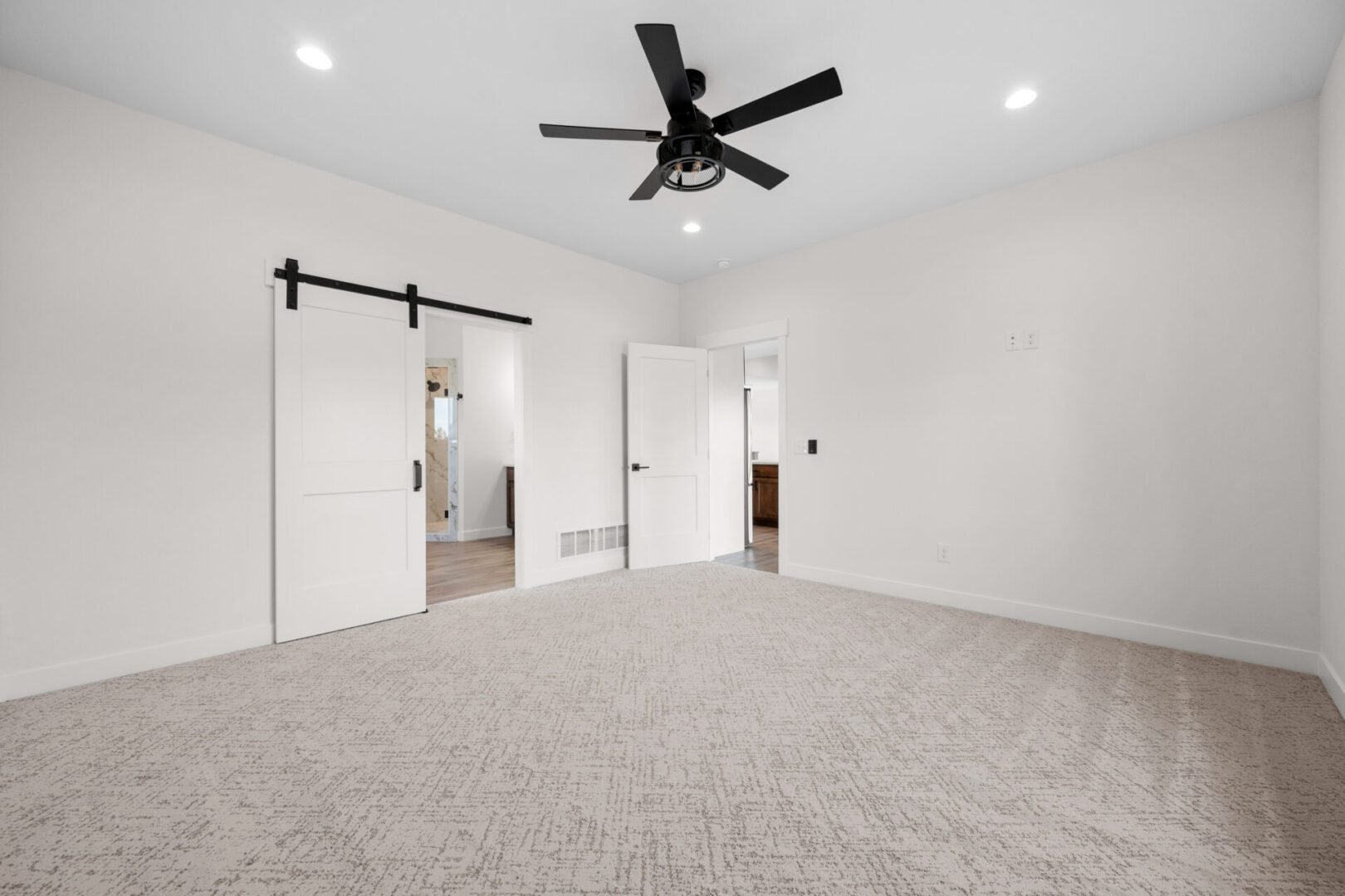 Spacious empty bedroom with beige carpet and black ceiling fan.