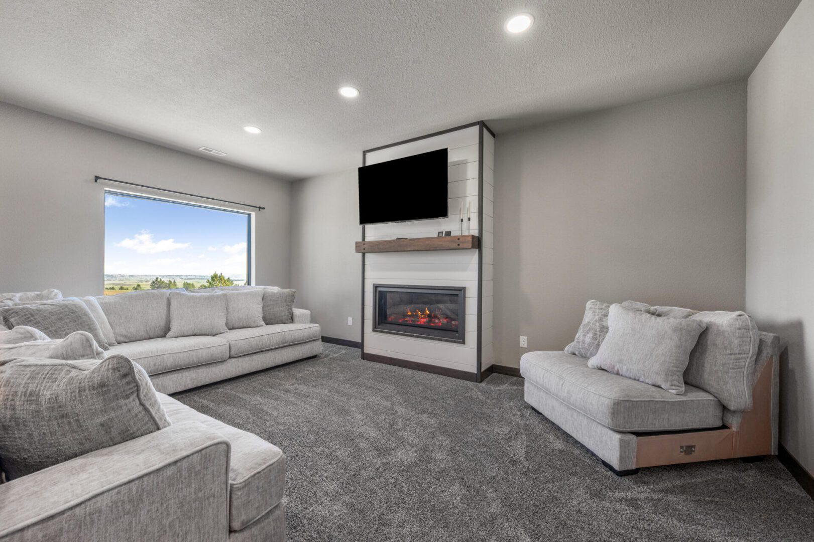 Modern living room with gray carpet, white couches, and a wall-mounted TV above a fireplace.