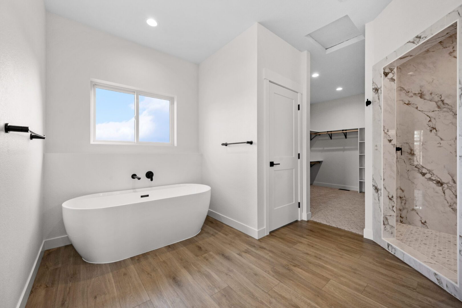 Modern bathroom with a white freestanding tub and wood-look flooring.