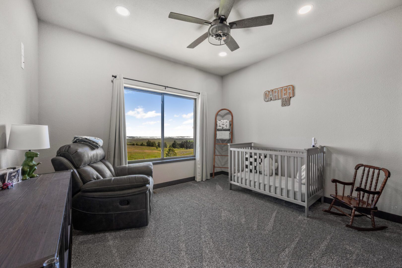 Bright nursery with a crib, recliner, and large window overlooking a scenic view.